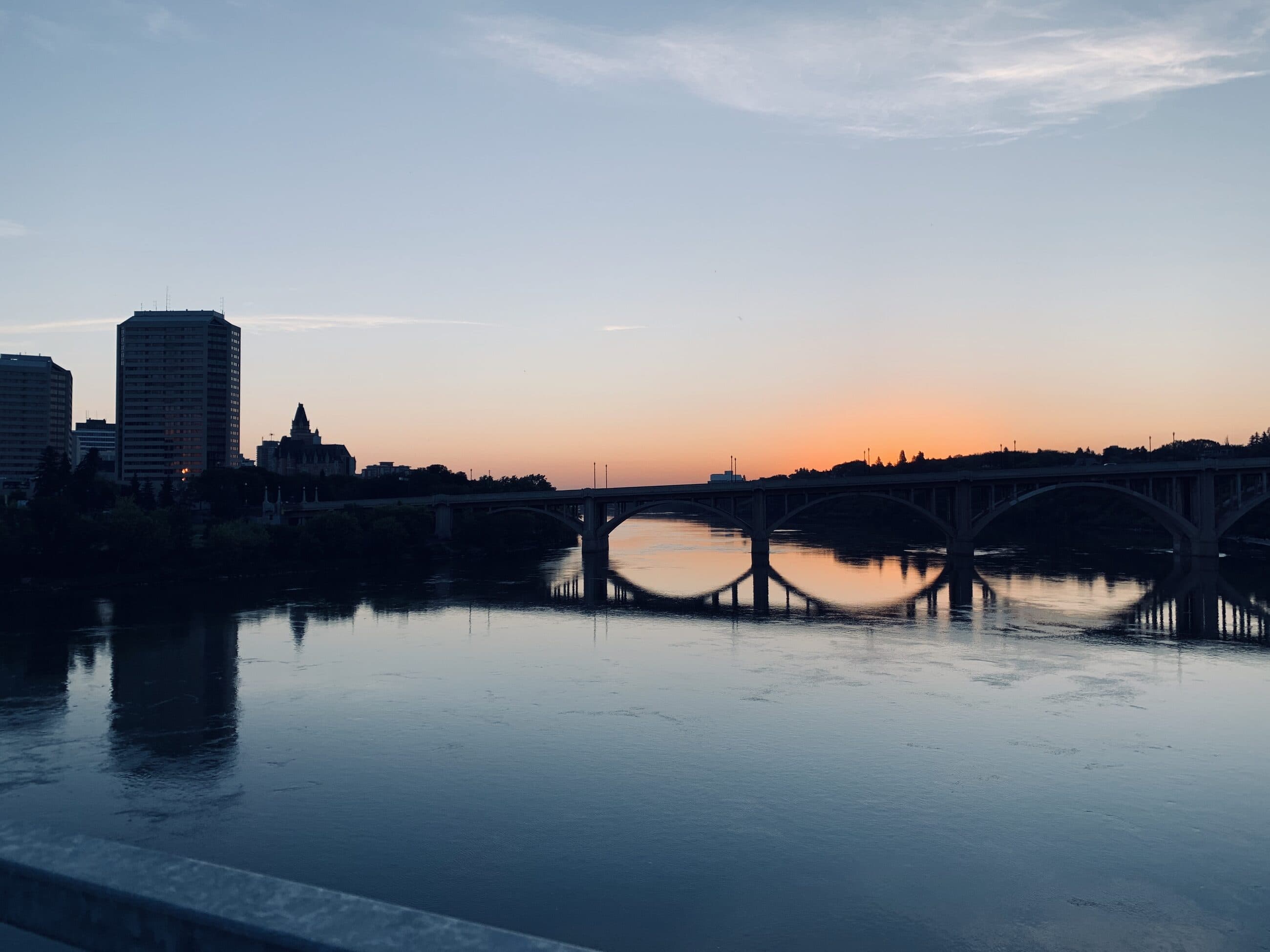The South Saskatchewan River and a bridge at dusk in Saskatoon, with an amber strip on the horizon